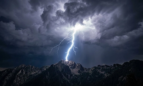 Lightning striking a mountain peak beneath dark storm clouds