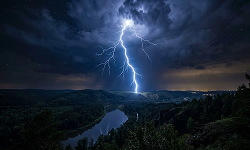 Lightning striking over a forested river valley during a nighttime thunderstorm