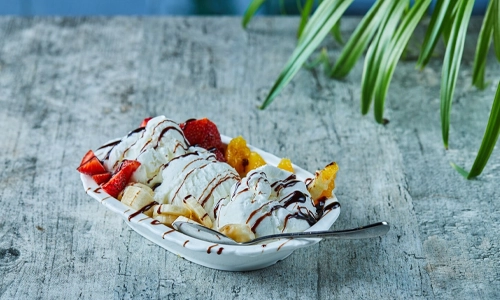 Ice cream sundae topped with strawberries, banana, orange and syrup