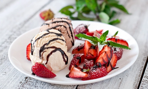Ice cream with strawberries and chocolate on a white plate