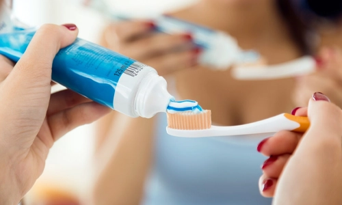 close-up of hands pressing and laying paste in a tooth brush.