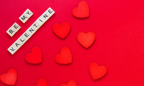 “Be My Valentine” text on Wooden tiles decorated with red heart on a red background