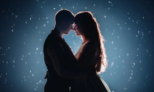 romantic just married couple hugging face to face against illuminated dark background with glowing sparkles around.